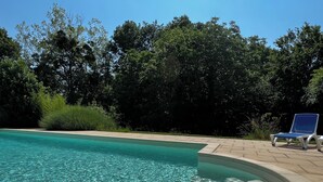 A swimming pool with clear water, surrounded by a tiled deck and a lounge chair.