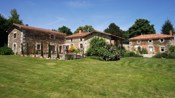 A stone building with a tiled roof, surrounded by a well-maintained lawn and trees.