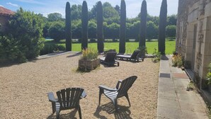 An outdoor seating area with chairs and a table, surrounded by a gravel path and greenery.