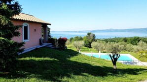 A house with a swimming pool, surrounded by greenery and a clear view of the sea.