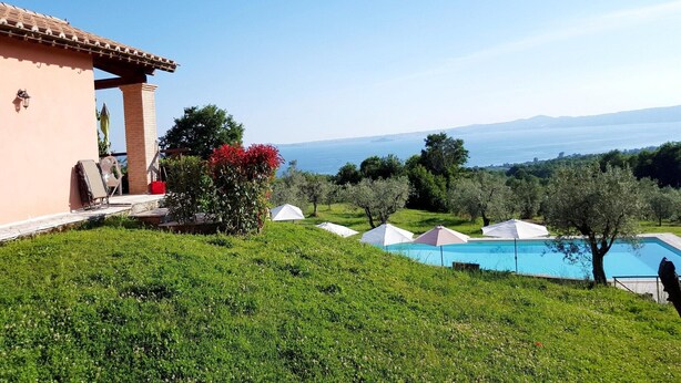 A pool area with umbrellas, a building with a tiled roof, and a view of the sea.