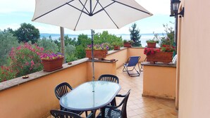 A balcony with a table and chairs, a large umbrella, and potted plants.
