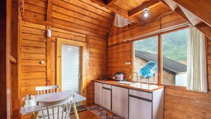 A wooden cabin interior with a kitchen area, a dining table with chairs, and a window with a view of the outdoors. - Diamond Cabin House (Dieng Kulon)