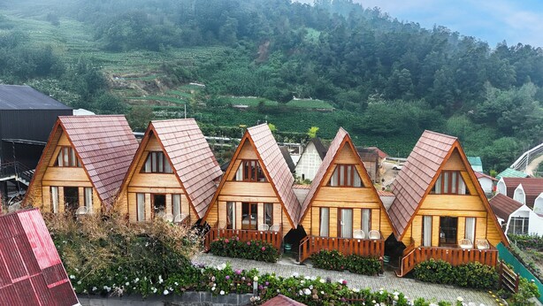 A row of wooden cabins with pitched roofs, surrounded by lush greenery and terraced fields in the background. - Diamond Cabin House (Dieng Kulon)