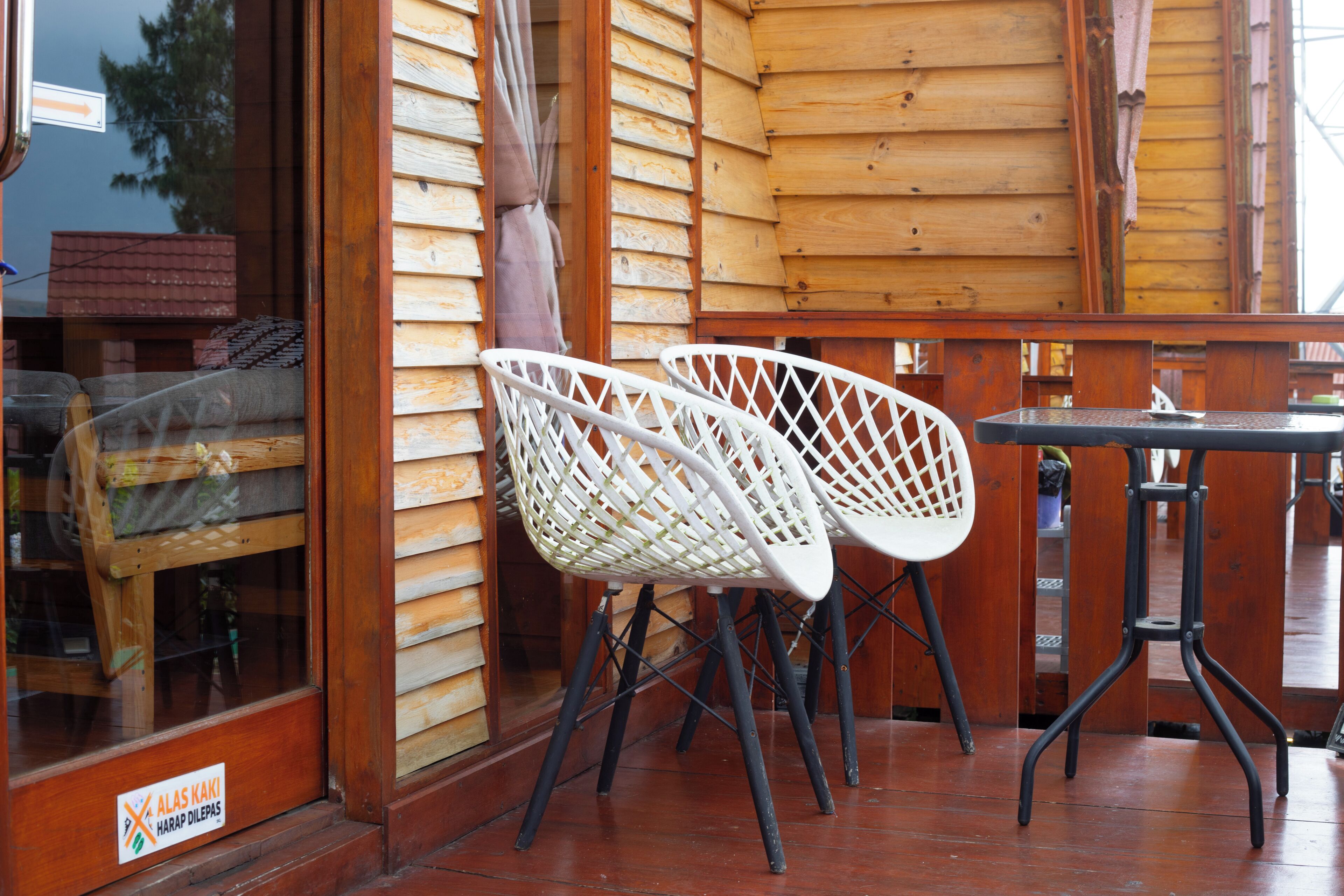 Fachada de madeira com duas cadeiras brancas e uma mesa pequena, porta de vidro com uma placa e um deck de madeira.