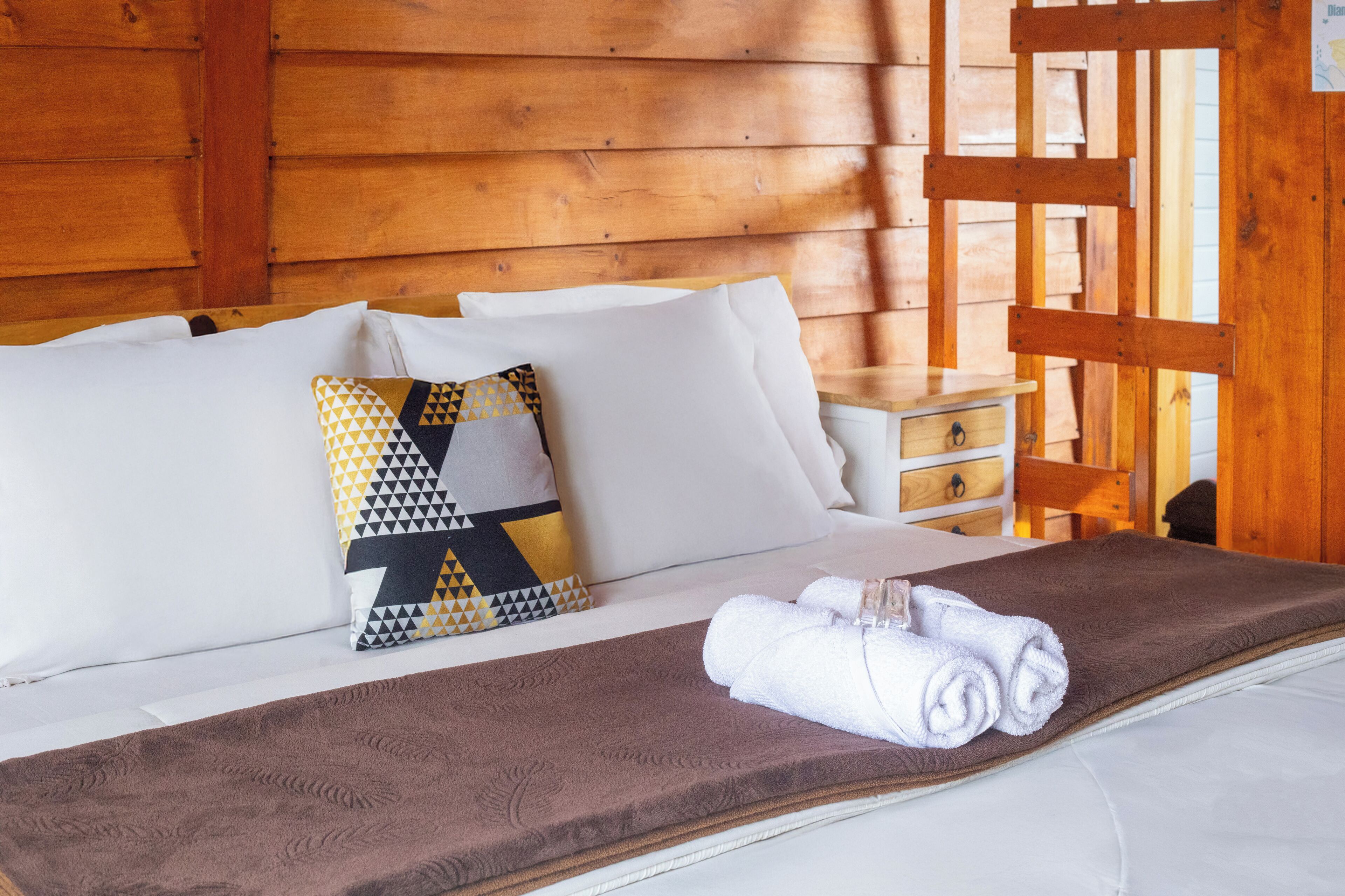 A neatly made bed with white linens, a brown blanket, and a patterned pillow.