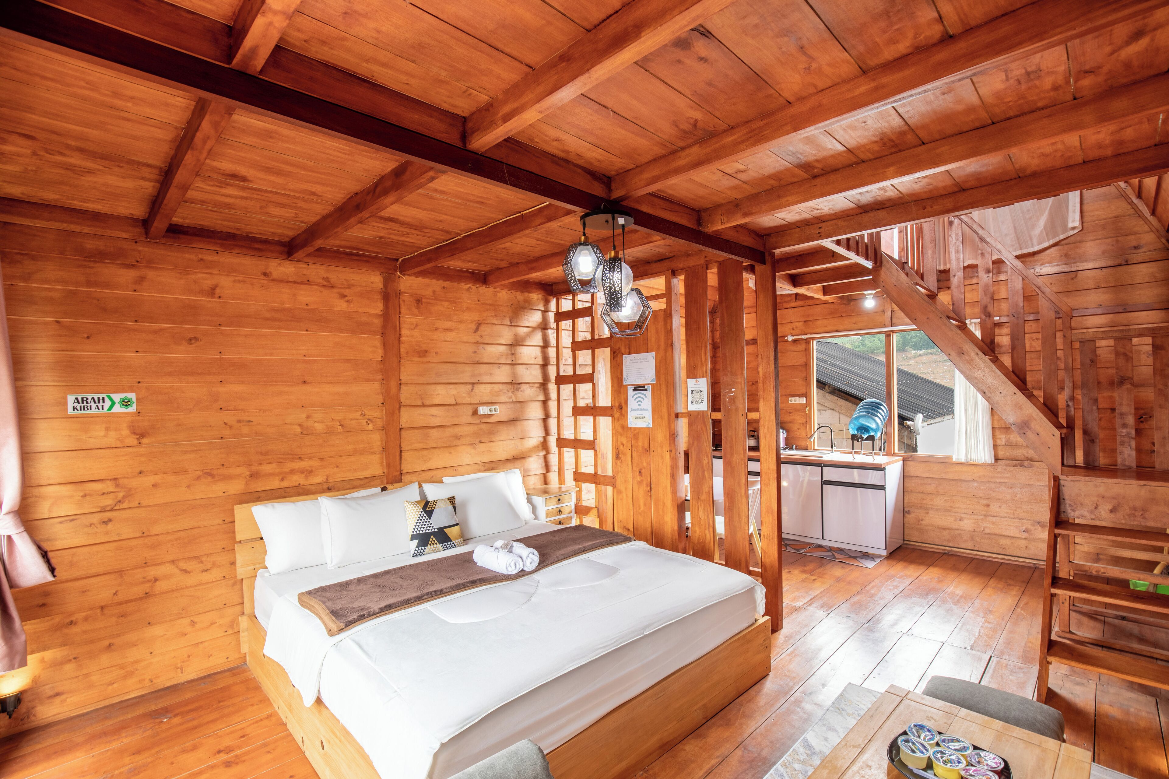 Een houten hut met een bed, een kitchenette en een trap.