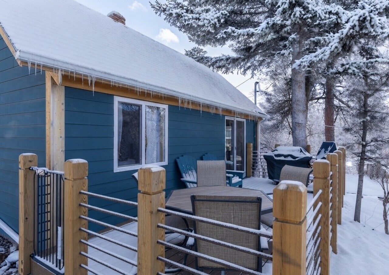 A wooden deck with a metal railing, a covered outdoor seating area, and a snow-covered landscape.