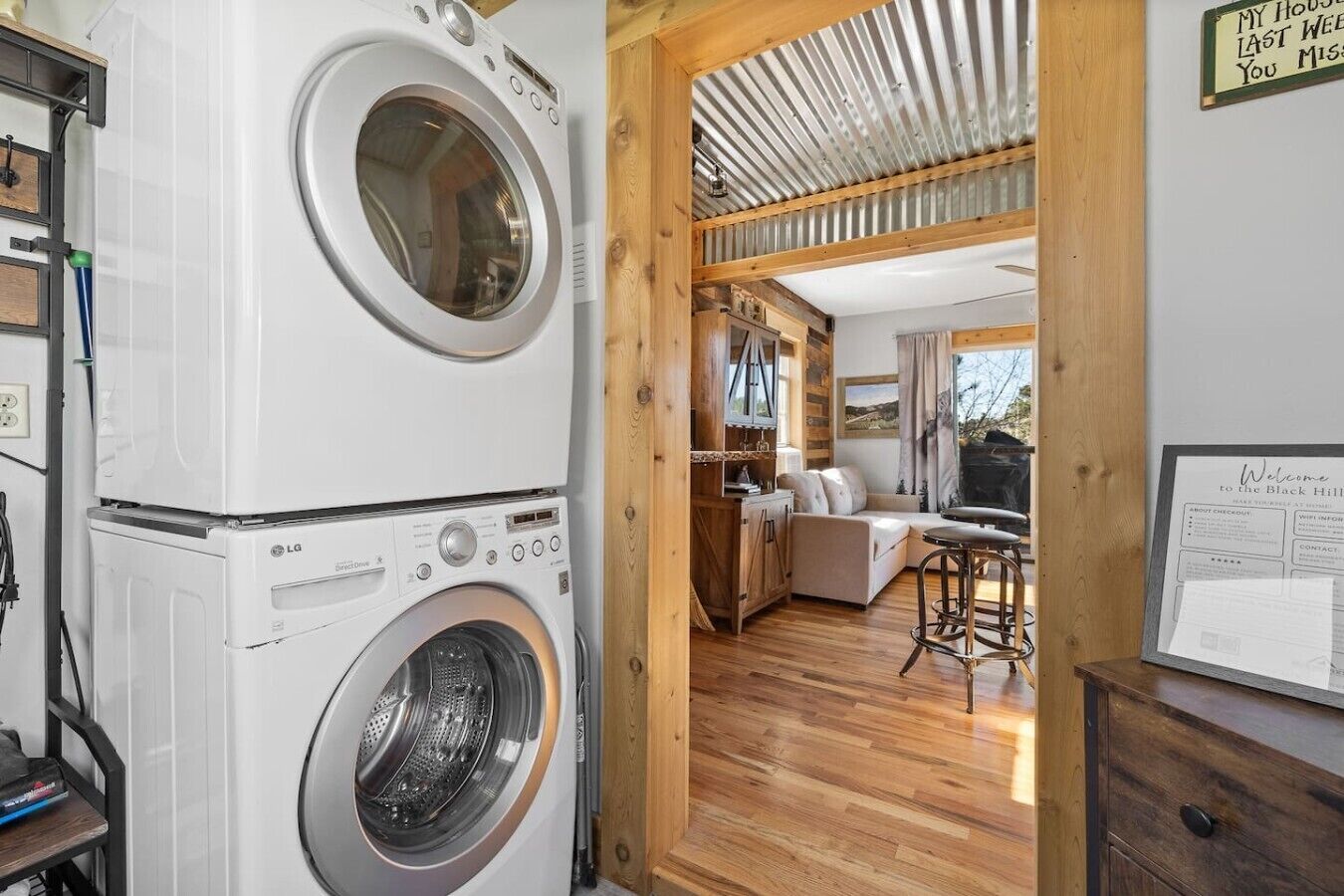 Een wasserette met gestapelde wasmachines en drogers, een houten interieur, een zithoek met een bank en tafel, en een bord aan de muur.