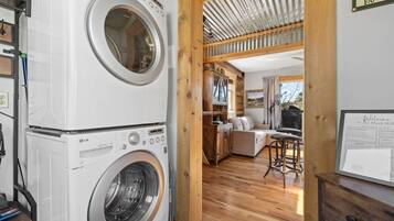 Een wasserette met gestapelde wasmachines en drogers, een houten interieur, een zithoek met een bank en tafel, en een bord aan de muur.