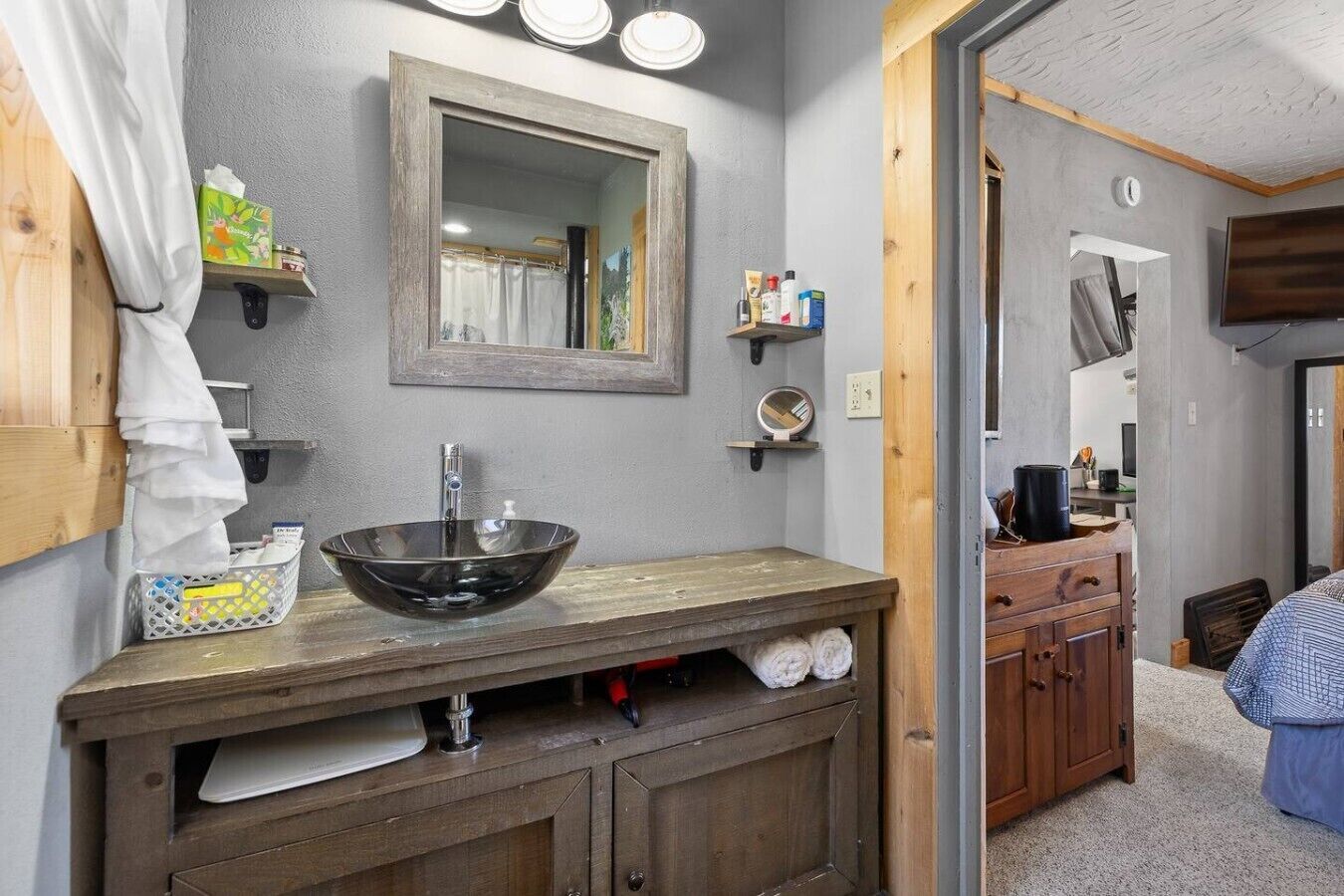 A bathroom with a wooden vanity, a large mirror, and a glass bowl sink.
