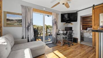 Un salon moderne comprenant un canapé, un bureau avec un ordinateur, un téléviseur à écran plat et un ventilateur de plafond.