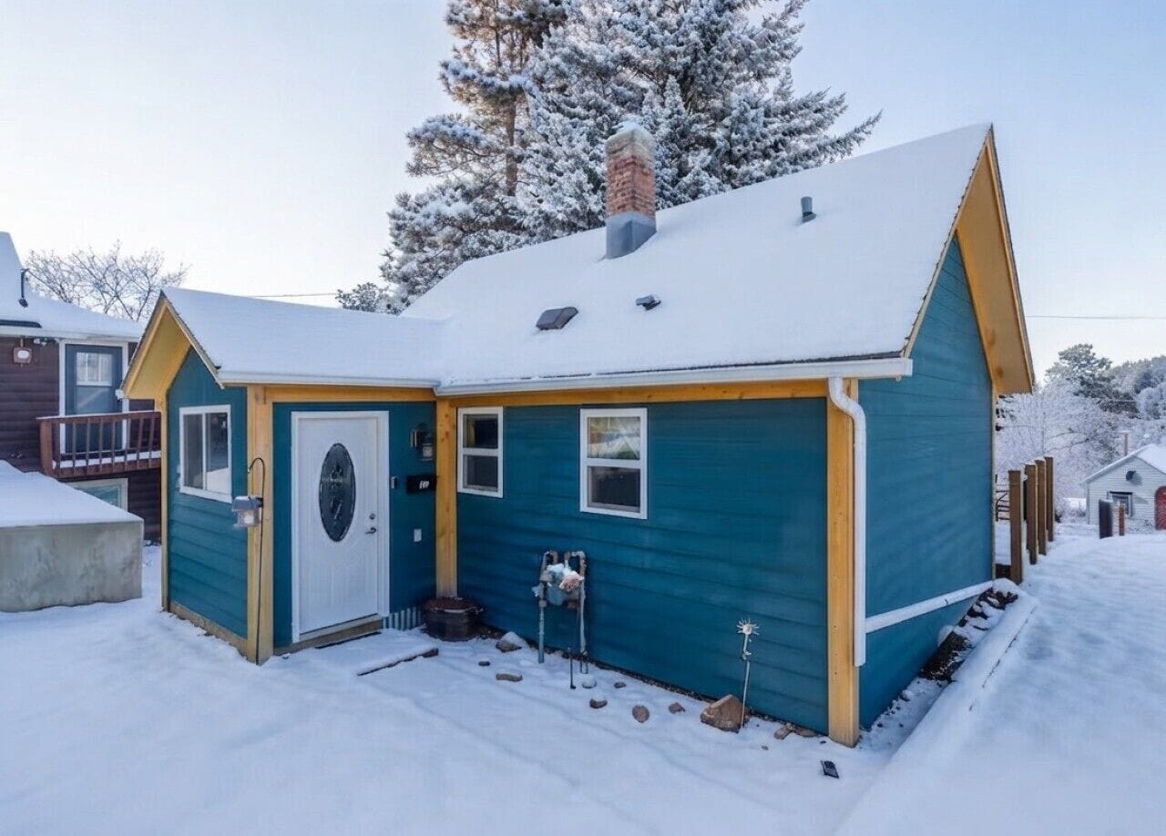 Una casa pequeña de un solo piso con techo nevado y puerta principal.