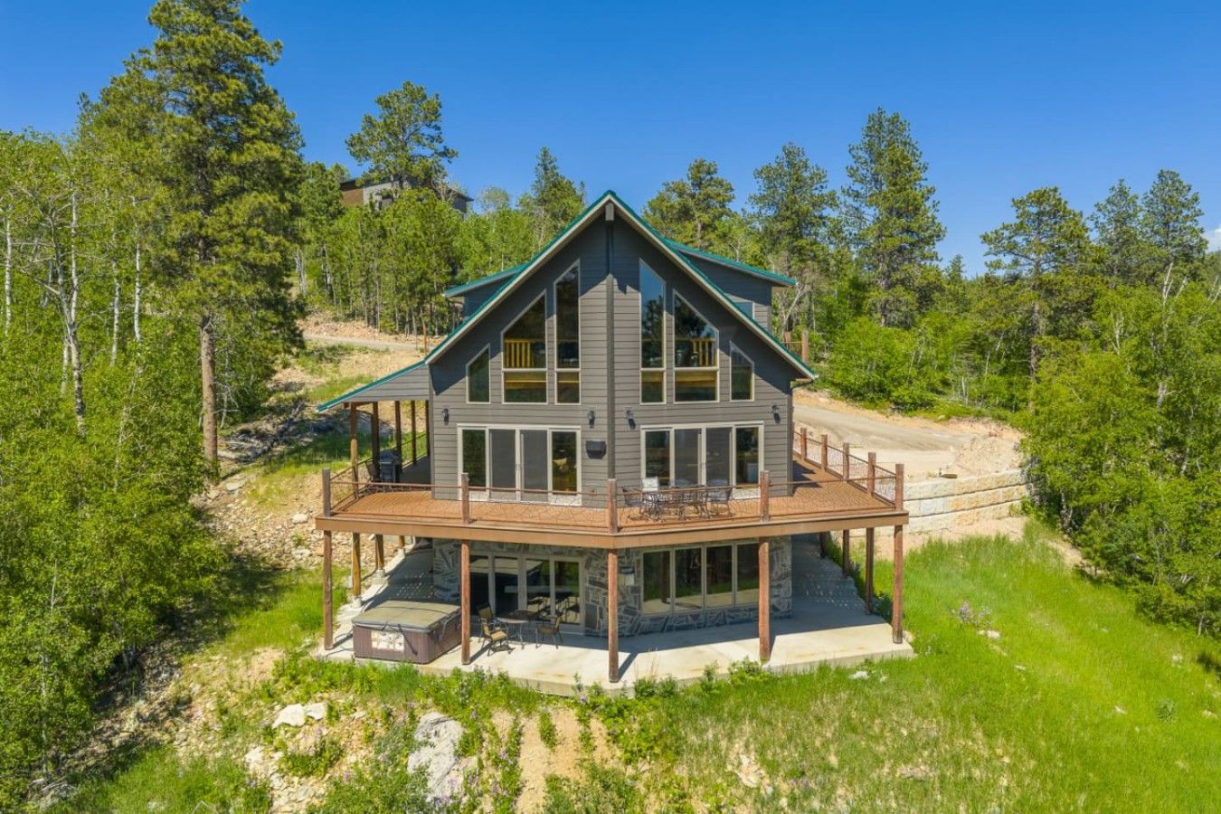 A two-story wooden house with a deck, surrounded by trees.