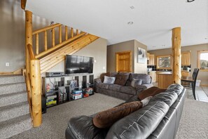 Ein Wohnzimmer mit grauem Sofa, einer Holztreppe und einem Flachbildfernseher.