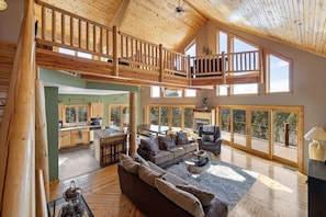 Un vaste espace de vie de style loft, doté d’un plafond haut, de poutres en bois, d’une mezzanine, de grandes fenêtres et d’une cuisine avec des armoires en bois.