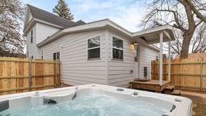Une maison avec un jacuzzi dans le jardin, une clôture en bois et un patio couvert.