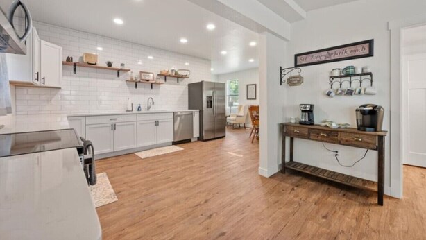 Une cuisine moderne avec des meubles blancs, un plancher en bois et un coin café.