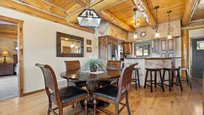A wooden dining table with chairs, a kitchen area with wooden cabinets, and a hanging light fixture. - Golf Course, Sleeps 12, Garage (Sturgis)
