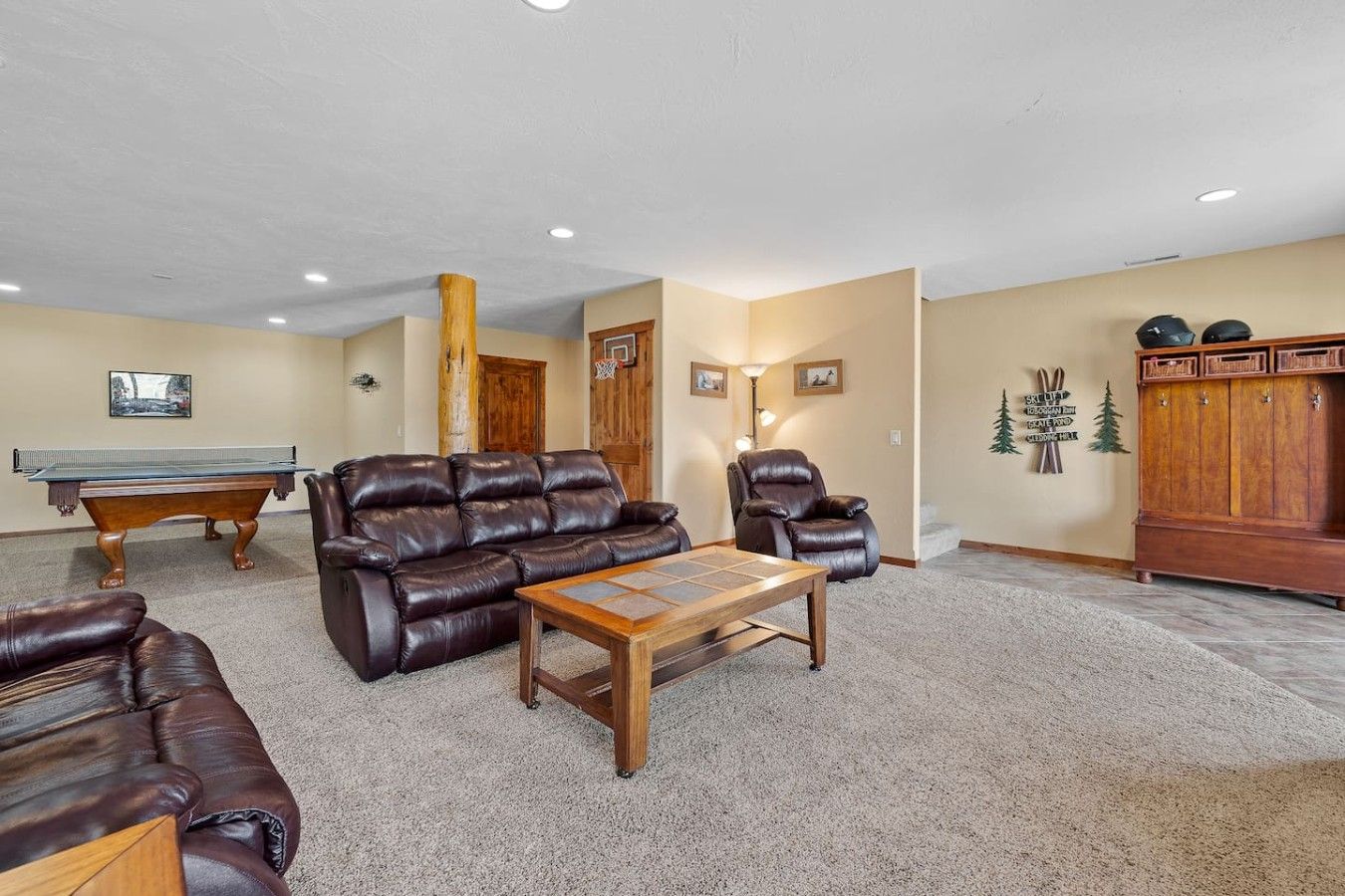 A living room with a pool table, leather sofas, a wooden coffee table, and a cabinet.