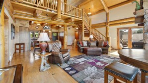 A spacious living room with a wooden staircase, leather furniture, and a large rug. - Golf Course, Sleeps 12, Garage (Sturgis)