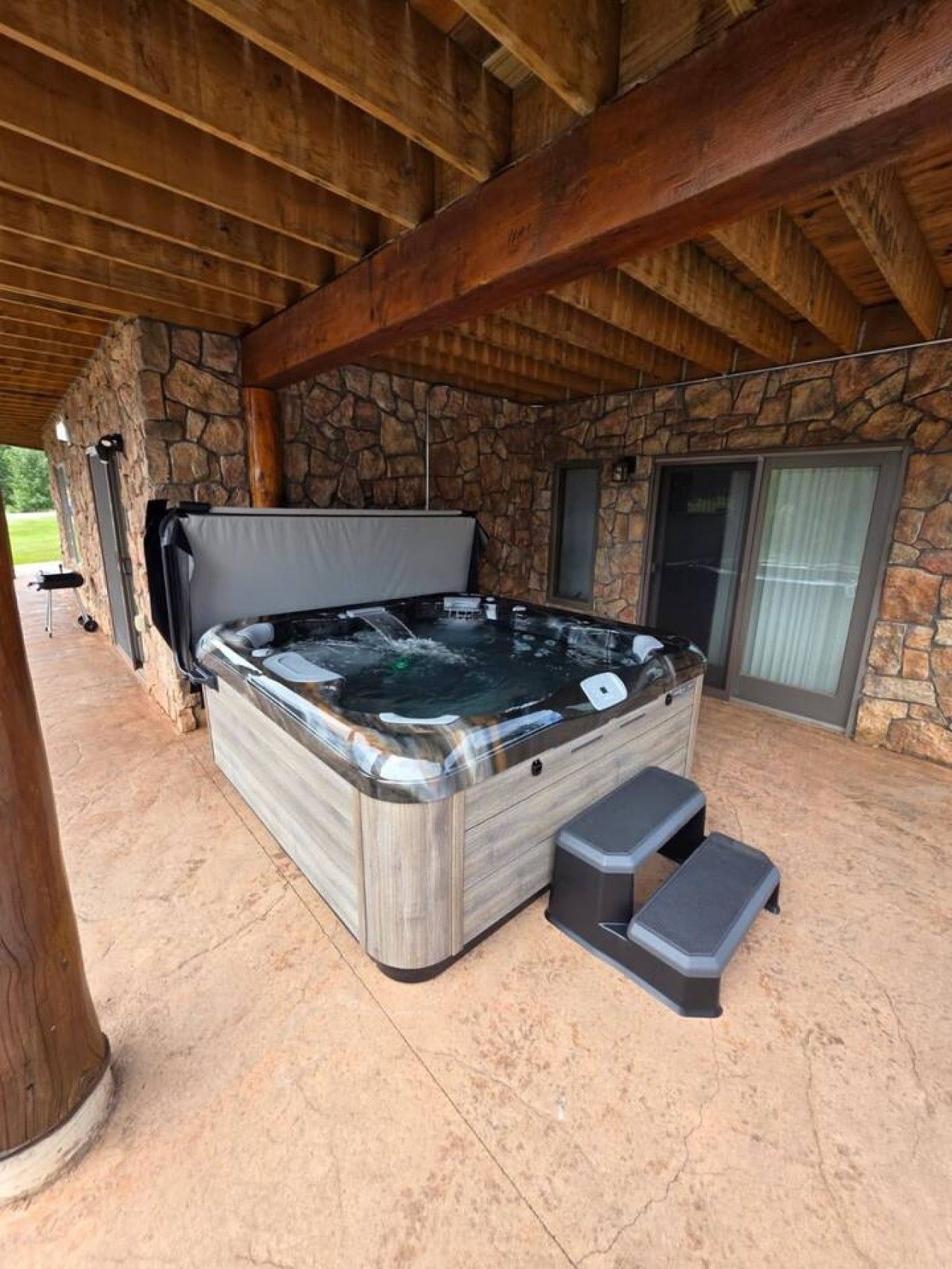 A hot tub in a covered outdoor area with stone walls and a wooden ceiling.