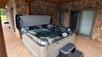 A hot tub in a covered outdoor area with stone walls and a wooden ceiling.