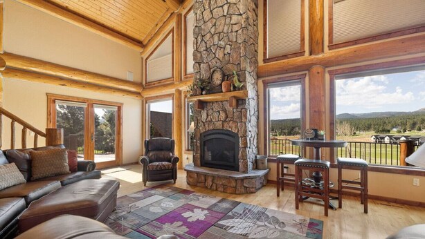 A spacious living room with a stone fireplace, leather furniture, and large windows offering a view of the outdoors. - Golf Course, Sleeps 12, Garage (Sturgis)