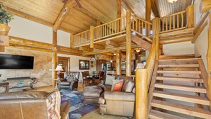 A spacious living area with a wooden staircase, a flat-screen TV, leather furniture, and a dining area. - Golf Course, Sleeps 12, Garage (Sturgis)