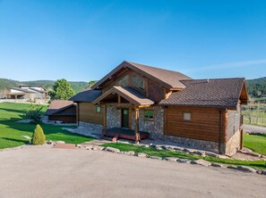 A two-story log cabin with a stone foundation, a front porch, and a clear view of the surrounding landscape. - Golf Course, Sleeps 12, Garage (Sturgis)