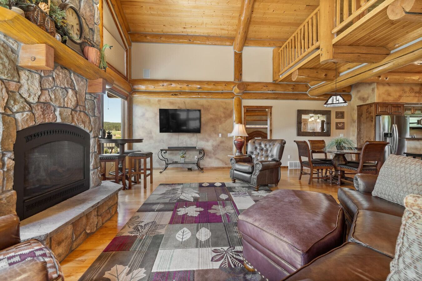 A spacious living room with a stone fireplace, leather furniture, and a large TV.