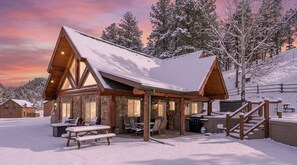 Een lodge met een sneeuwbedekt dak, stenen muren en een terras met buitenmeubels.