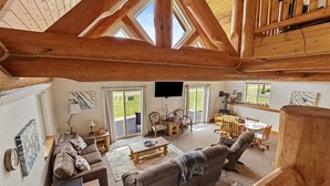 Amplia sala de estar con techo alto, vigas de madera, chimenea y un gran ventanal corredero que da a un espacio exterior.