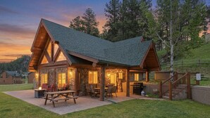Una cabaña con fachada de piedra, un porche cubierto y una zona de barbacoa.