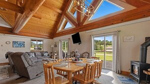 Un salón amplio con techo alto, vigas de madera, chimenea y un gran ventanal con vistas al exterior.