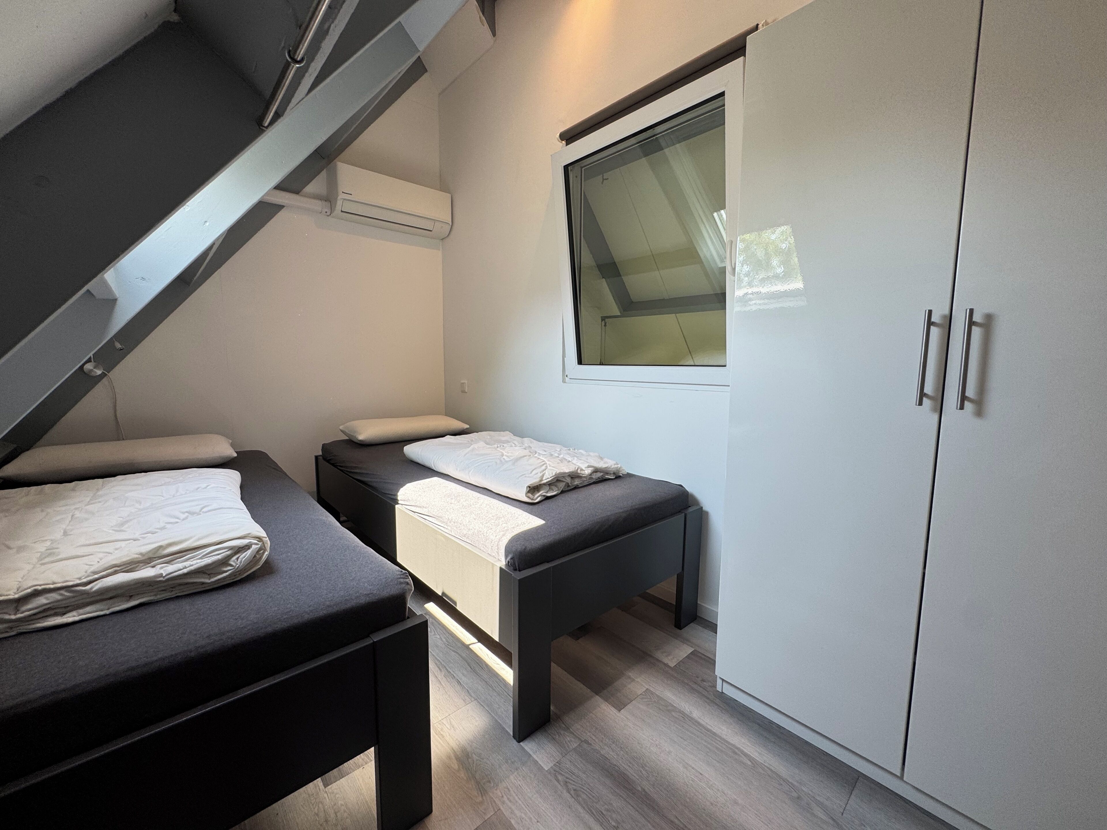 Een slaapkamer met een stapelbed, nachtkastje, kledingkast en een raam.