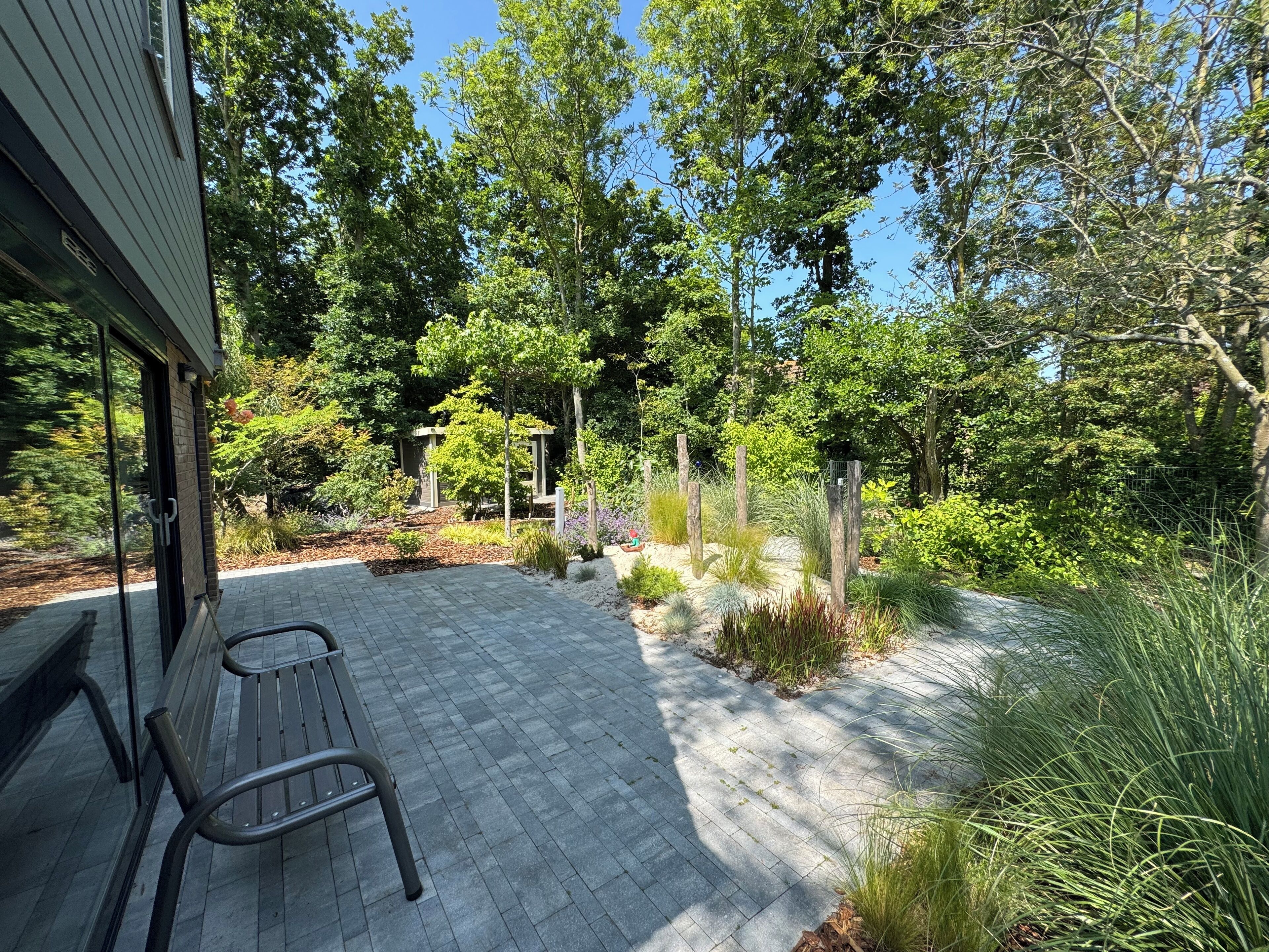 A patio area with a bench, surrounded by a garden with various plants and trees.