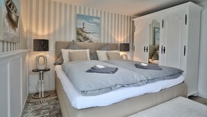 Une chambre à coucher avec un grand lit, un papier peint à rayures, un tableau représentant un phare et une armoire.