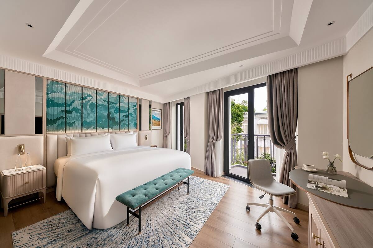 Habitación de hotel moderna con una cama grande, un banco, un escritorio y vistas al exterior.