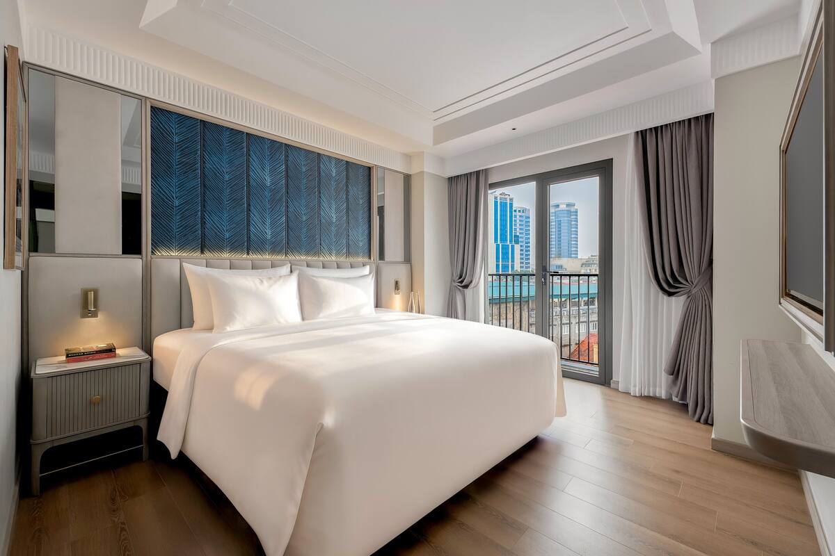 Un hotel moderno con una cama grande, una mesita de noche, un espejo y vistas de la ciudad a través de la ventana.