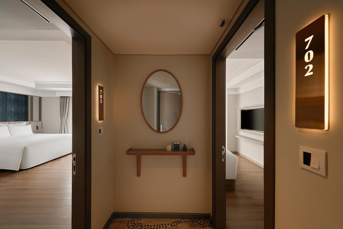 Pasillo de hotel con una cama, un espejo, un estante y una puerta con el número 702.