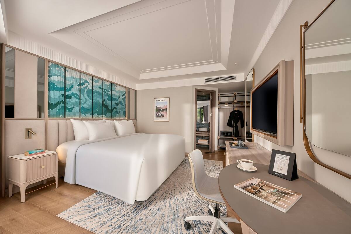 Habitación de hotel moderna con una cama grande, un escritorio con silla, un espejo y vistas a la ciudad.