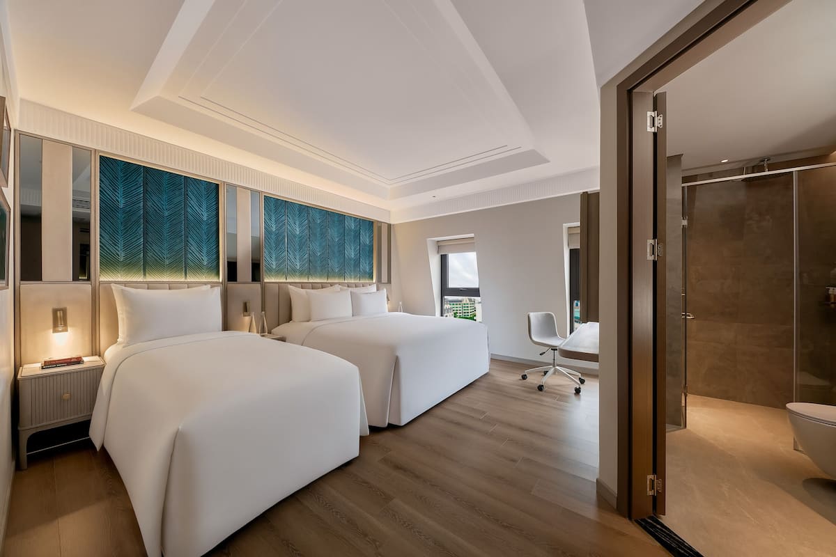 Una habitación de hotel moderna con dos camas grandes, un escritorio y zona de ducha.