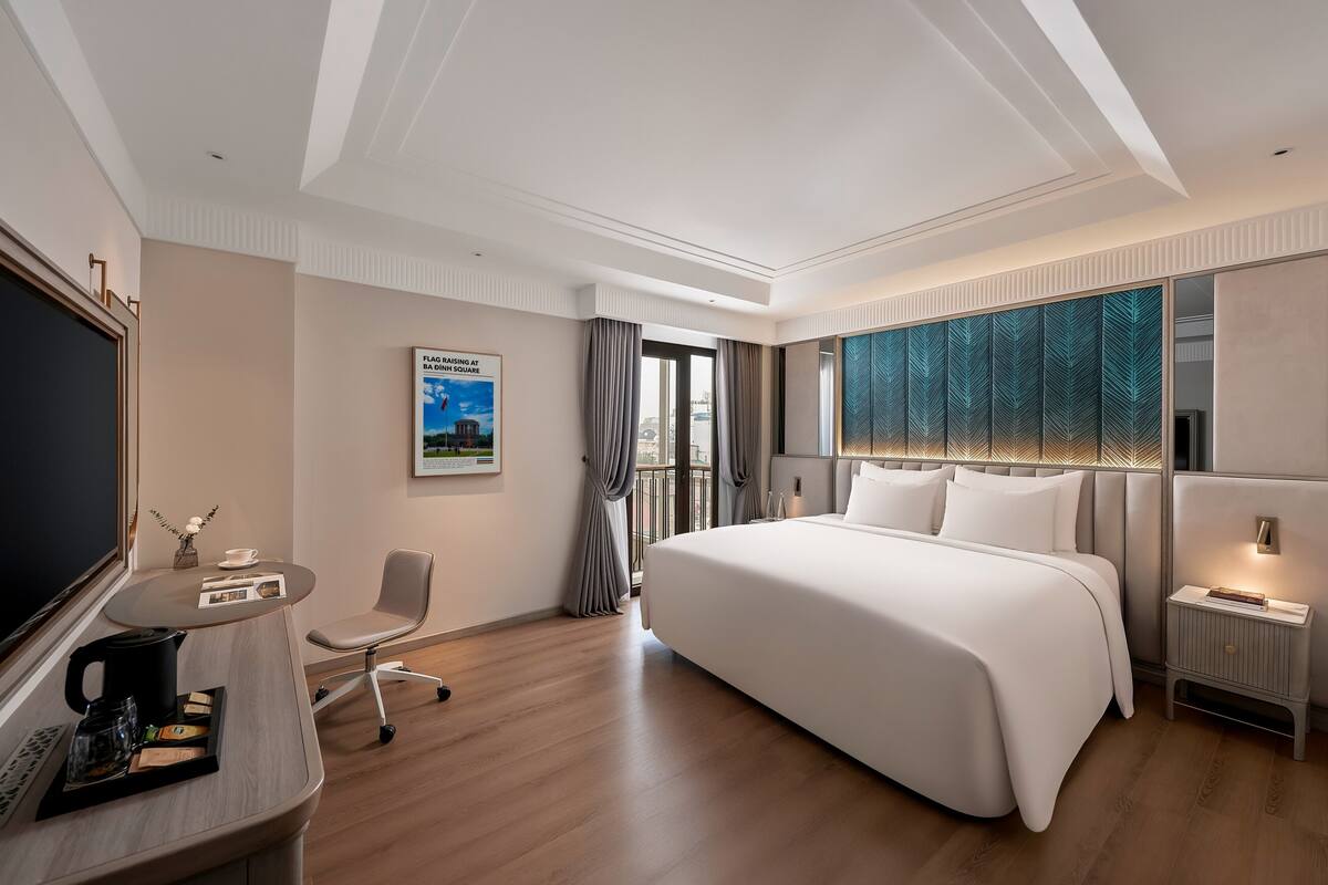Una habitación de hotel moderna con una cama grande, un escritorio con cafetera, una silla y un televisor.