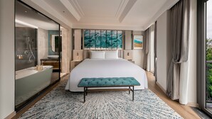 Een moderne hotelkamer met een groot bed, een zithoek, een badkamer met bad en een groot raam met gordijnen.