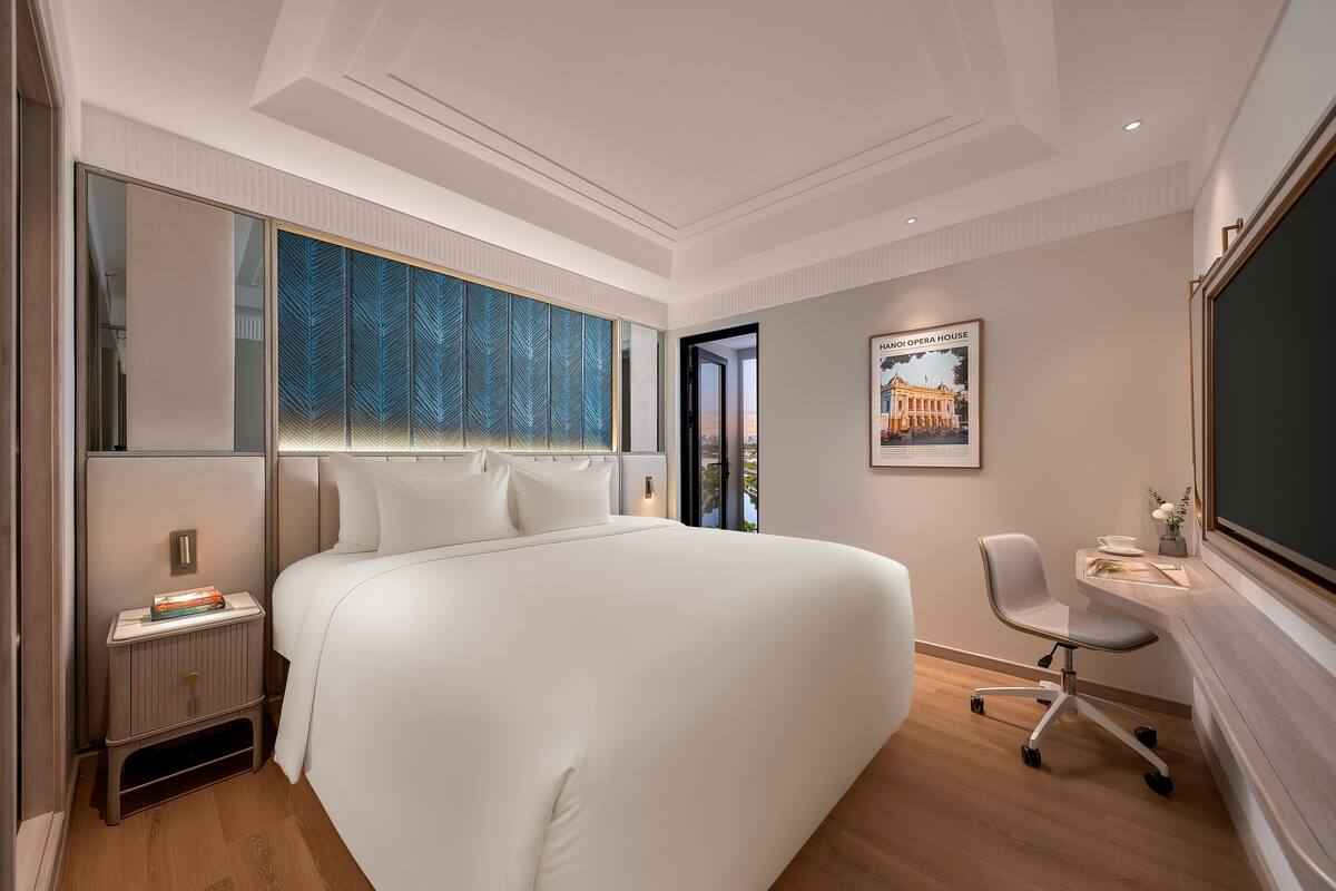 Una habitación de hotel moderna con una cama grande, un escritorio con una silla, un espejo amplio y un cuadro en la pared.