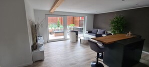 A modern kitchen with a wooden countertop, a dining area with a table and chairs, and a sliding glass door leading to an outdoor patio. - Modern vacation bungalow in the Neuhof forest settlement on the Großer Wünsdorfer See lake (Zossen (Neuhof))