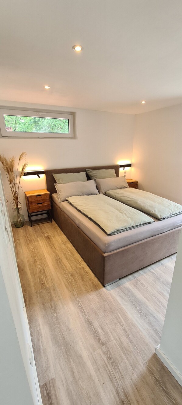 A modern bedroom with a large bed, bedside tables, a window, and recessed ceiling lights. - Modern vacation bungalow in the Neuhof forest settlement on the Großer Wünsdorfer See lake (Zossen (Neuhof))