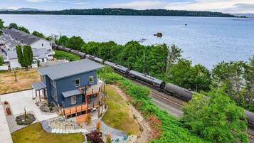 A modern two-story house with a balcony, located near a waterfront with a train passing by.