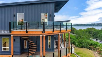 A modern two-story house with a glass balcony, a spiral staircase, and a view of a lake.